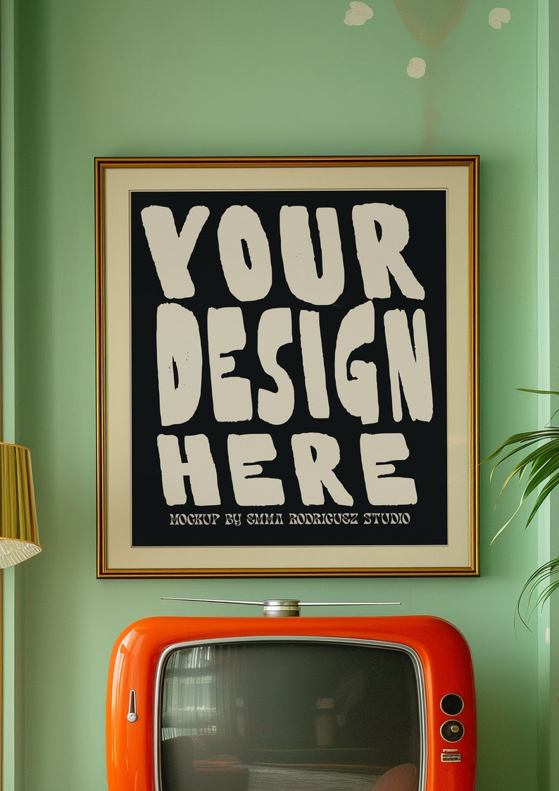 May include: A framed poster with a black background and white text that reads "YOUR DESIGN HERE" with the words "MOCKUP BY EMMA RODRIGUEZ STUDIO" below the text. The poster is hanging on a green wall above a vintage orange television.