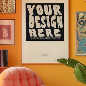 May include: A framed poster with a black background and white text that reads "YOUR DESIGN HERE" with the words "MOCKUP BY EMMA RODRIGUEZ STUDIO" below. The poster is hanging on a yellow wall with a pink armchair in the foreground.