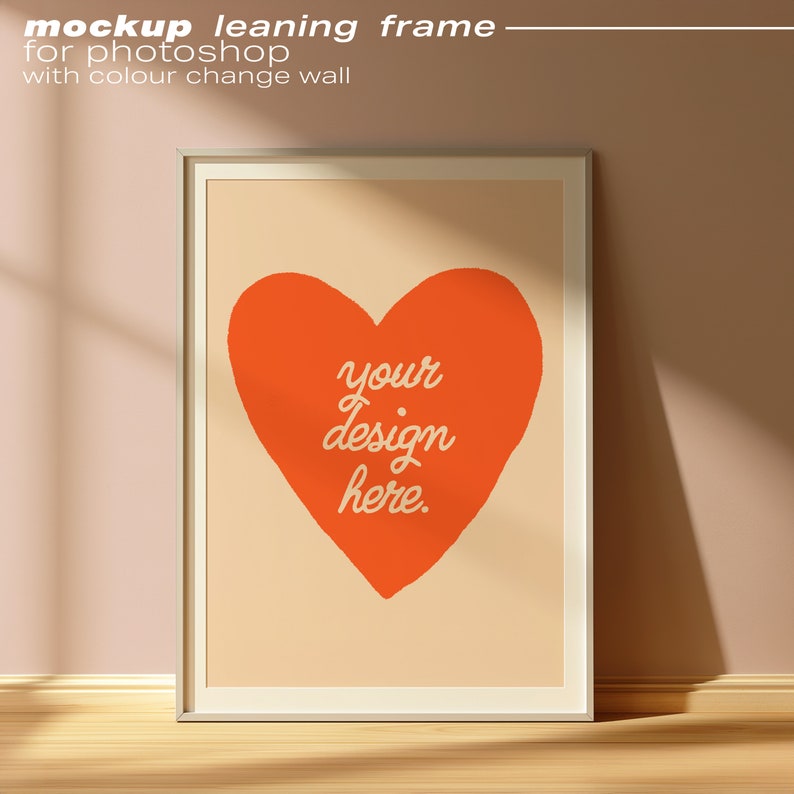 May include: A white frame leaning against a peach wall with a peach background and a red heart with the text "your design here" inside the heart.