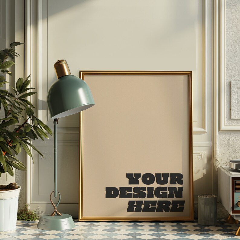 以下が含まれることがあります： ベージュの背景に「YOUR DESIGN HERE」という黒い文字が書かれた、金色の額縁に入ったポスター。ポスターは白い壁に立てかけられており、手前に緑色のランプと鉢植えの植物がある。
