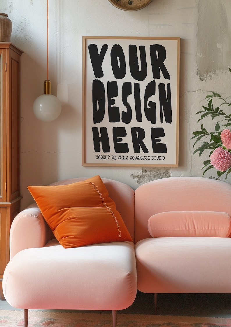 May include: A pink velvet sofa with an orange velvet pillow and a framed poster that says "YOUR DESIGN HERE" with the text "MOCKUP BY EMILI RODRIGUEZ STUDIO" below it.