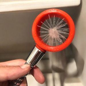 Peut inclure: Un outil de nettoyage rouge et argent avec une tête de brosse. La tête de brosse a un design circulaire avec des poils humides qui semblent être faits de matière douce.