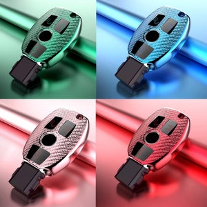 May include: Four key fobs with different coloured cases. The cases are green, blue, pink, and red. Each case has a textured pattern and a silver metal finish. The key fobs have four buttons and a black plastic base.
