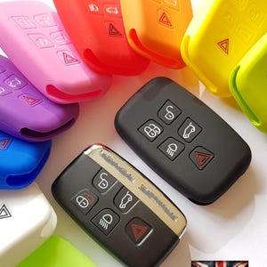 May include: Assortment of colorful silicone key covers for a car key fob. The key covers are in various colors, including pink, purple, blue, green, yellow, orange, and red. The key covers are designed to protect the car key fob from scratches and wear. The key covers are also available in a black silicone option.