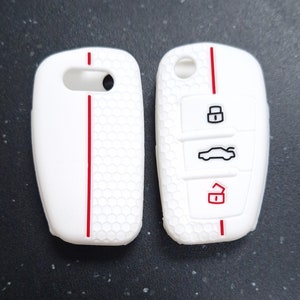 May include: Two white car key fobs with a red stripe down the centre. The fob on the right has black icons for lock, unlock, and car. The fobs have a honeycomb pattern.