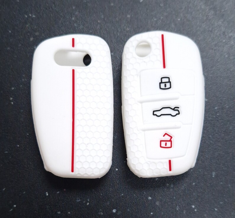 May include: Two white car key fobs with a red stripe down the centre. The fob on the right has black icons for lock, unlock, and car. The fobs have a honeycomb pattern.