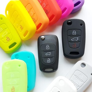 May include: Assortment of colourful silicone key covers for car keys. The covers are in various colours, including yellow, orange, pink, purple, blue, green, and white. The covers are designed to protect car keys from scratches and wear.