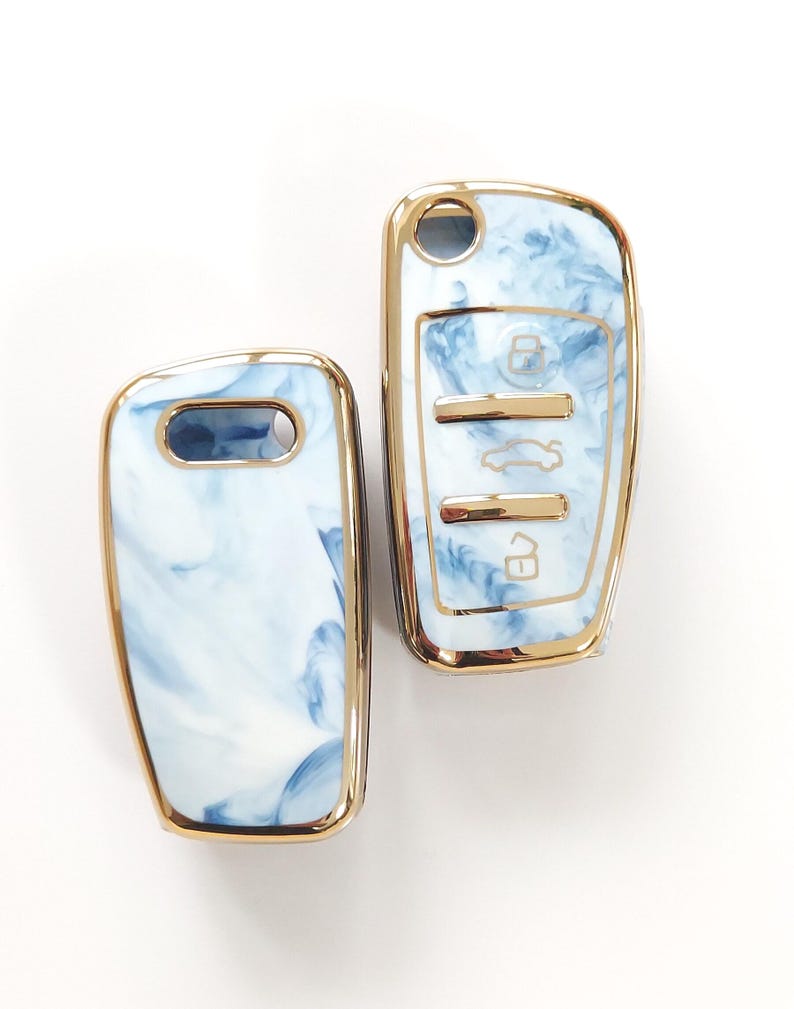 May include: Two car key fobs with a blue and white marbled design. The key fobs have a gold-colored trim. One fob has a key ring hole, and the other has buttons for locking, unlocking, and other car functions.