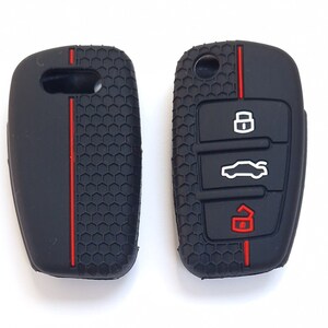 May include: Two black car key fobs. The fob on the left has a red stripe. The fob on the right has three white icons and a red icon. Both fobs have a textured, honeycomb pattern.
