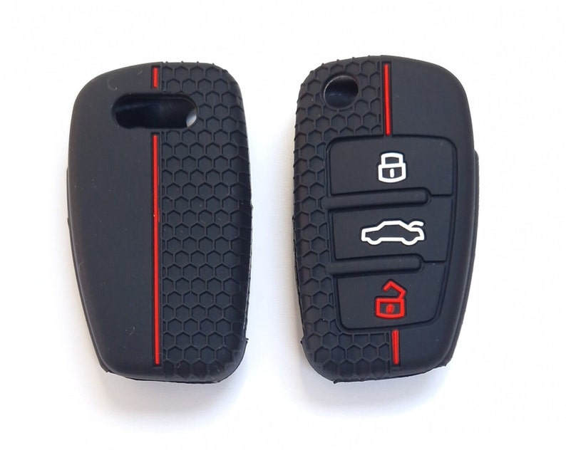 May include: Two black car key fobs. The fob on the left has a red stripe. The fob on the right has three white icons and a red icon. Both fobs have a textured, honeycomb pattern.