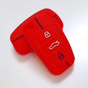 May include: Two red silicone car key covers. The covers have a textured honeycomb pattern and feature white icons for lock, unlock, and boot release. The key covers are designed to protect car keys.