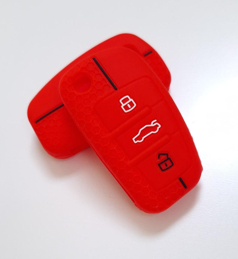 May include: Two red silicone car key covers. The covers have a textured honeycomb pattern and feature white icons for lock, unlock, and boot release. The key covers are designed to protect car keys.