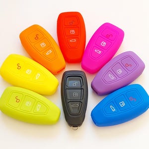 Peut inclure: Un ensemble de sept housses de clés en silicone de différentes couleurs, notamment jaune, vert, bleu, violet, rose, orange et noir. Les housses sont conçues pour s'adapter aux porte-clés de voiture et les protéger des rayures et des dommages.