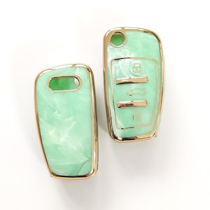 May include: Two car key fobs with a mint green marbled design and gold-colored trim. One fob has key symbols. The other has a key ring hole. The fobs are set against a white background.