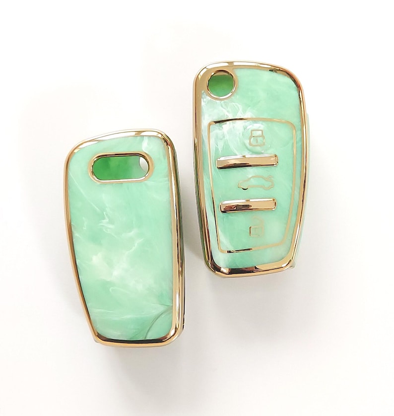 May include: Two car key fobs with a mint green marbled design and gold-colored trim. One fob has key symbols. The other has a key ring hole. The fobs are set against a white background.