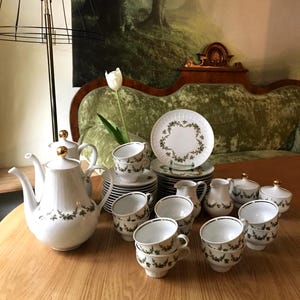 Könnte beinhalten: Ein weißes Porzellan-Tee-Set mit grünem Blumenmuster. Das Set beinhaltet eine Teekanne, eine Milchkännchen, eine Zuckerdose und 12 Tassen und Untertassen.