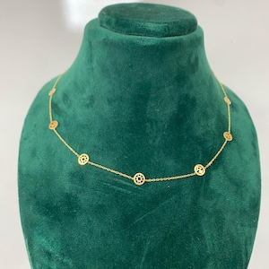 Può includere: Una delicata collana d'oro con una serie di ciondoli circolari con intricati disegni traforati. La collana è esposta su un busto di velluto verde, che mostra i suoi dettagli raffinati e la sua maestria.