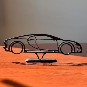 May include: A black metal silhouette of a sports car on a black stand. The car is on a wooden surface.