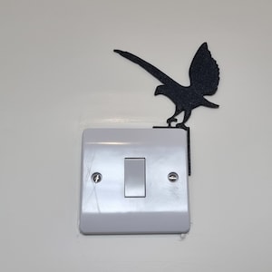 Puede incluir: Un interruptor de luz blanco con una silueta negra de un pájaro posado encima.