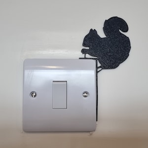 Puede incluir: Un interruptor de luz blanco con una silueta negra de una ardilla en la parte superior.
