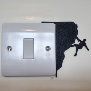 May include: A white light switch with a black silhouette of a person rock climbing on a cliff. The silhouette is attached to the right side of the light switch.