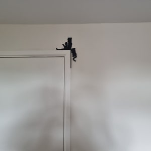 May include: A white door with a black silhouette of a person climbing a wall, with a black silhouette of a person riding a bicycle on the wall above the door.
