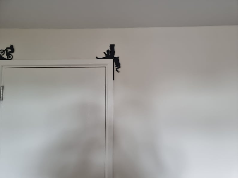 May include: A white door with a black silhouette of a person climbing a wall, with a black silhouette of a person riding a bicycle on the wall above the door.