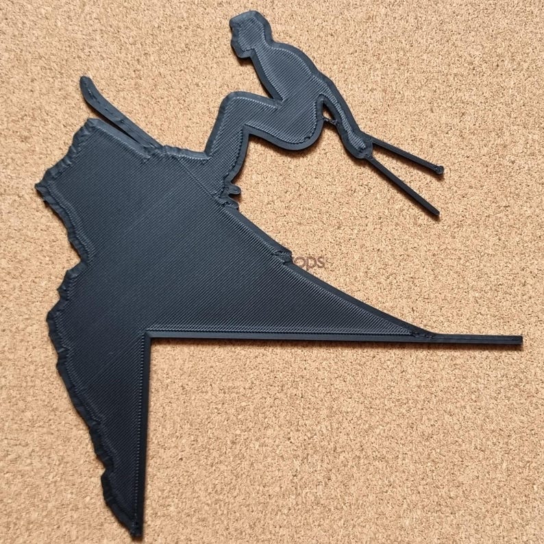 Op de afbeelding: Een zwarte 3D-geprinte ski&euml;rfiguur in een afdalingshouding. De ski&euml;r staat op een helling, met skistokken uitgestrekt. De figuur is een silhouet, met een getextureerd oppervlak.