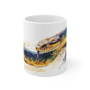 May include: A white ceramic mug with a watercolor illustration of a snake with a yellow, black, and blue pattern. The snake's tongue is extended and the background is a watercolor wash of blue, yellow, and white.