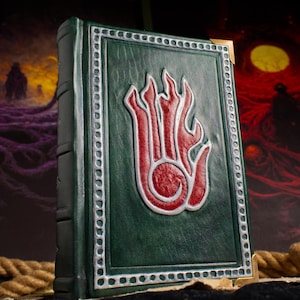 May include: A green leather-bound journal with a silver embossed hand with flames on the front cover.