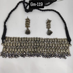 May include: A silver-toned necklace and earring set. The necklace features a paisley design with dangling beads. The earrings have a similar design with a bell-shaped drop. The necklace is attached to a black cord. The text "Gm-119" is in the top left corner.
