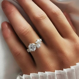 Puede incluir: Un anillo de oro con un gran diamante redondo y diamantes más pequeños engastados en un diseño de racimo.