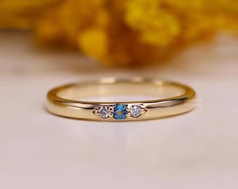 May include: A delicate gold band ring with three small gemstones. The center stone is a blue sapphire, and the two stones on either side are white diamonds.