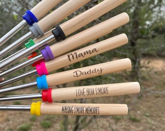May include: A set of eight wooden roasting sticks with colorful silicone handles. The sticks are engraved with different messages, including "Mama", "Daddy", "Love You S'more", and "Making S'more Memories".