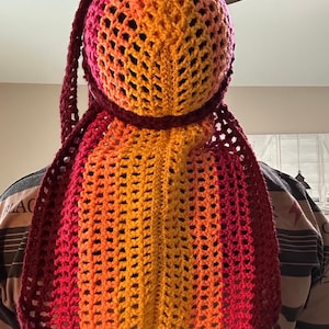 May include: A crocheted hooded scarf in shades of red, orange, and yellow. The scarf is made with a mesh pattern and has a long, flowing design.