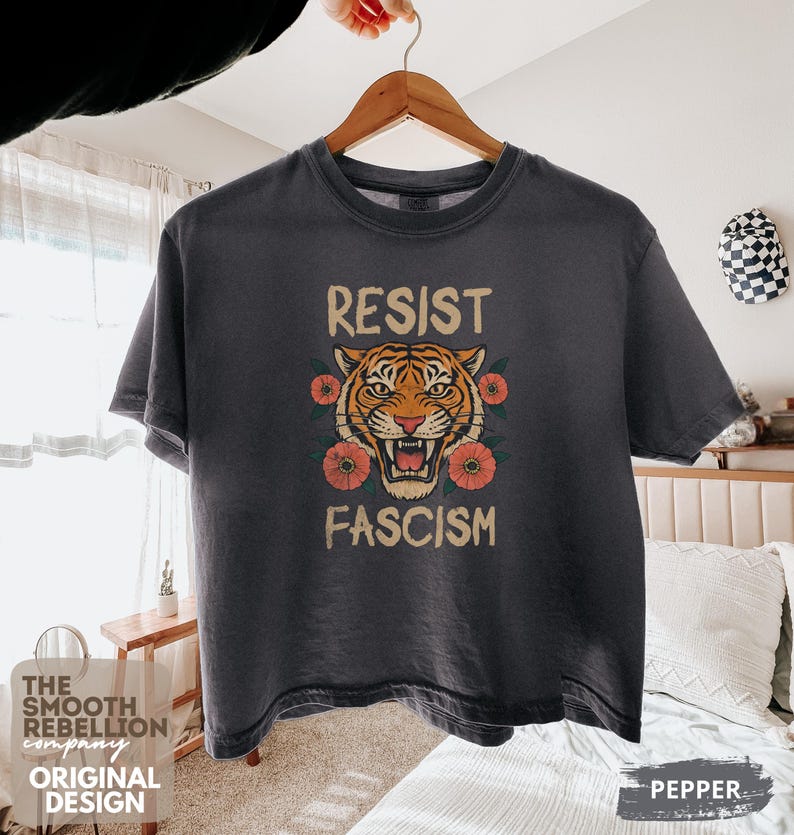 RESIST FASCISM Tiger Boxy T-Shirt for women. Political Protest Graphic Tee. Boxy tee that features a vintage-style painted tiger surrounded by vibrant poppies. Perfect for protests, marches, or just everyday defiance. Political merch for making a statement. Anti Trump top made for the loud and the politically engaged. Whether you're fighting fascism, defending democracy, or just making a statement. Short sleeves, crew neck. Boxy cropped tee. Very soft fabric. Printed in the US.