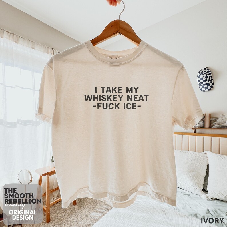 Ivory Comfort Colors boxy tee. The shirt has bold black text reading “I TAKE MY WHISKEY NEAT – FUCK ICE –.” Slightly Cropped. Boxy, relaxed fit. 100% Cotton. Heavy Fabric. Protest & Anti Ice Apparel.