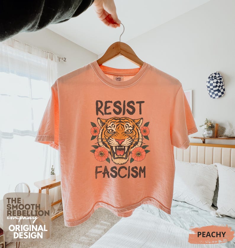 RESIST FASCISM Tiger Boxy T-Shirt for women. Political Protest Graphic Tee. Boxy tee that features a vintage-style painted tiger surrounded by vibrant poppies. Perfect for protests, marches, or just everyday defiance. Political merch for making a statement. Anti Trump top made for the loud and the politically engaged. Whether you're fighting fascism, defending democracy, or just making a statement. Short sleeves, crew neck. Boxy cropped tee. Very soft fabric. Printed in the US.