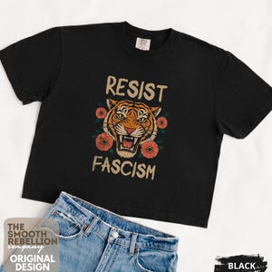 RESIST FASCISM Tiger Boxy T-Shirt for women. Political Protest Graphic Tee. Boxy tee that features a vintage-style painted tiger surrounded by vibrant poppies. Perfect for protests, marches, or just everyday defiance. Political merch for making a statement. Anti Trump top made for the loud and the politically engaged. Whether you're fighting fascism, defending democracy, or just making a statement. Short sleeves, crew neck. Boxy cropped tee. Very soft fabric. Printed in the US.