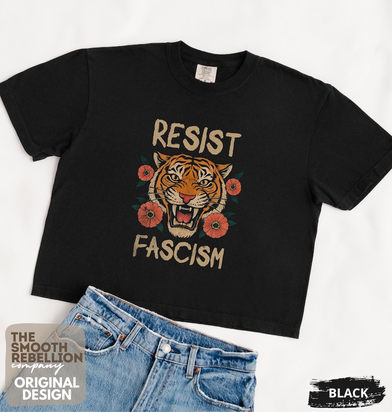 RESIST FASCISM Tiger Boxy T-Shirt for women. Political Protest Graphic Tee. Boxy tee that features a vintage-style painted tiger surrounded by vibrant poppies. Perfect for protests, marches, or just everyday defiance. Political merch for making a statement. Anti Trump top made for the loud and the politically engaged. Whether you're fighting fascism, defending democracy, or just making a statement. Short sleeves, crew neck. Boxy cropped tee. Very soft fabric. Printed in the US.