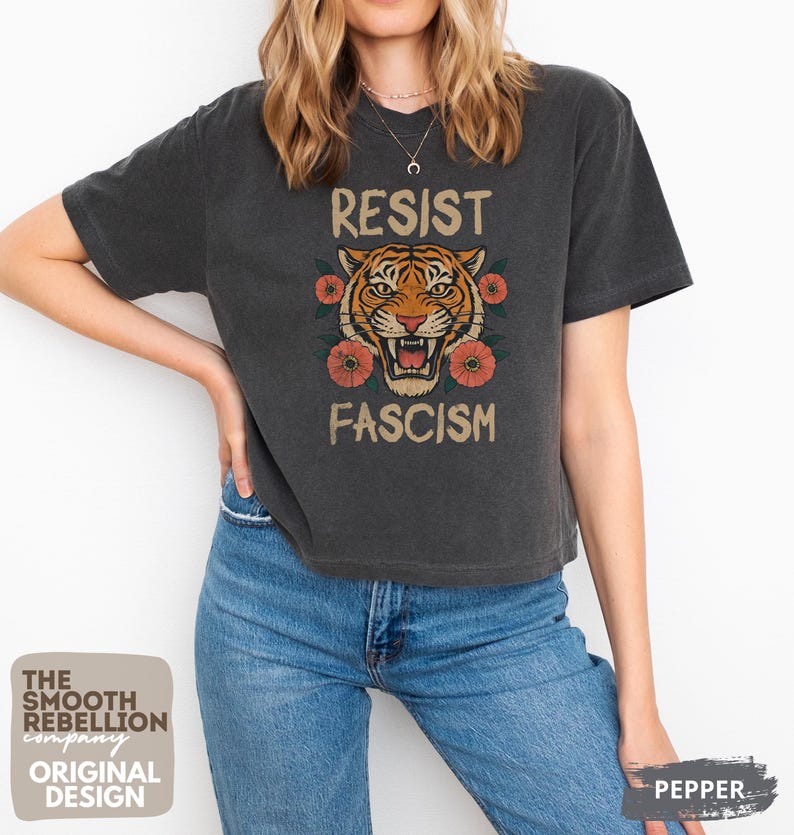 RESIST FASCISM Tiger Boxy T-Shirt for women. Political Protest Graphic Tee. Boxy tee that features a vintage-style painted tiger surrounded by vibrant poppies. Perfect for protests, marches, or just everyday defiance. Political merch for making a statement. Anti Trump top made for the loud and the politically engaged. Whether you're fighting fascism, defending democracy, or just making a statement. Short sleeves, crew neck. Boxy cropped tee. Very soft fabric. Printed in the US.