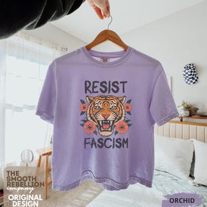 RESIST FASCISM Tiger Boxy T-Shirt for women. Political Protest Graphic Tee. Boxy tee that features a vintage-style painted tiger surrounded by vibrant poppies. Perfect for protests, marches, or just everyday defiance. Political merch for making a statement. Anti Trump top made for the loud and the politically engaged. Whether you're fighting fascism, defending democracy, or just making a statement. Short sleeves, crew neck. Boxy cropped tee. Very soft fabric. Printed in the US.