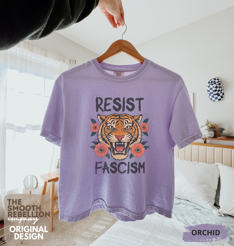 RESIST FASCISM Tiger Boxy T-Shirt for women. Political Protest Graphic Tee. Boxy tee that features a vintage-style painted tiger surrounded by vibrant poppies. Perfect for protests, marches, or just everyday defiance. Political merch for making a statement. Anti Trump top made for the loud and the politically engaged. Whether you're fighting fascism, defending democracy, or just making a statement. Short sleeves, crew neck. Boxy cropped tee. Very soft fabric. Printed in the US.