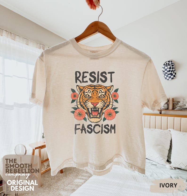 RESIST FASCISM Tiger Boxy T-Shirt for women. Political Protest Graphic Tee. Boxy tee that features a vintage-style painted tiger surrounded by vibrant poppies. Perfect for protests, marches, or just everyday defiance. Political merch for making a statement. Anti Trump top made for the loud and the politically engaged. Whether you're fighting fascism, defending democracy, or just making a statement. Short sleeves, crew neck. Boxy cropped tee. Very soft fabric. Printed in the US.