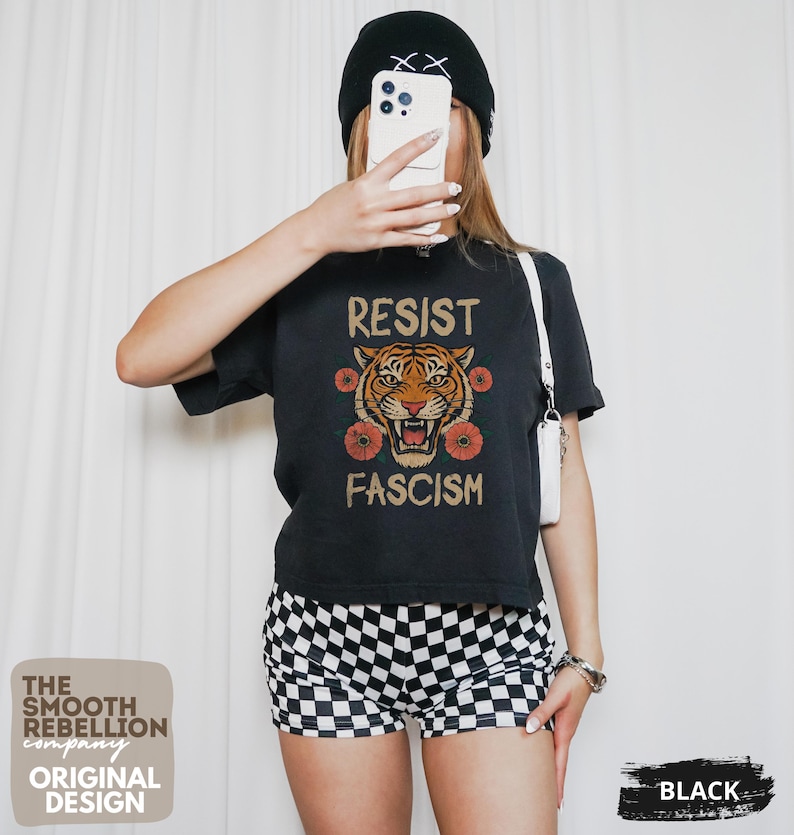 RESIST FASCISM Tiger Boxy T-Shirt for women. Political Protest Graphic Tee. Boxy tee that features a vintage-style painted tiger surrounded by vibrant poppies. Perfect for protests, marches, or just everyday defiance. Political merch for making a statement. Anti Trump top made for the loud and the politically engaged. Whether you're fighting fascism, defending democracy, or just making a statement. Short sleeves, crew neck. Boxy cropped tee. Very soft fabric. Printed in the US.