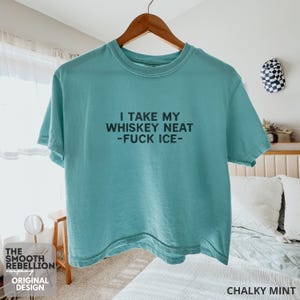 Mint Comfort Colors boxy tee. The shirt has bold black text reading “I TAKE MY WHISKEY NEAT – FUCK ICE –.” Slightly Cropped. Boxy, relaxed fit. 100% Cotton. Heavy Fabric. Protest & Anti Ice Apparel.