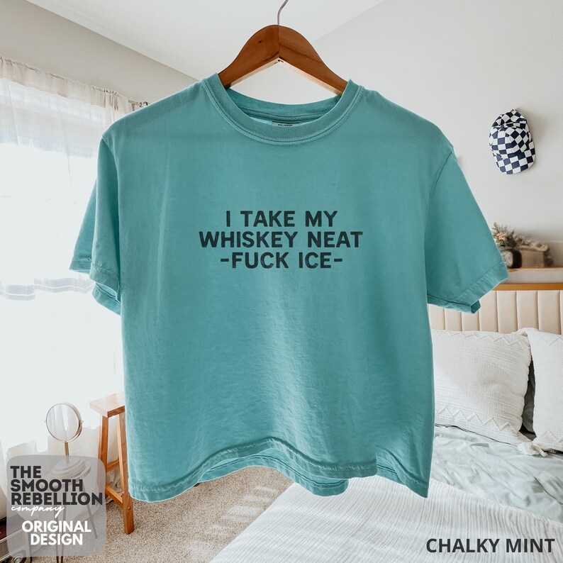 Mint Comfort Colors boxy tee. The shirt has bold black text reading “I TAKE MY WHISKEY NEAT – FUCK ICE –.” Slightly Cropped. Boxy, relaxed fit. 100% Cotton. Heavy Fabric. Protest & Anti Ice Apparel.