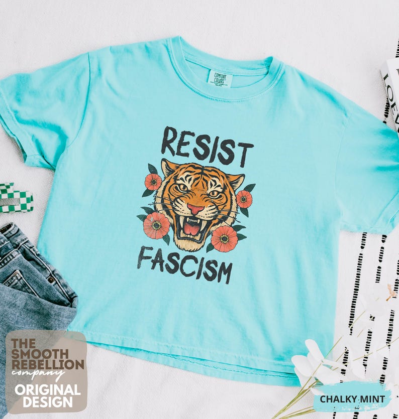 RESIST FASCISM Tiger Boxy T-Shirt for women. Political Protest Graphic Tee. Boxy tee that features a vintage-style painted tiger surrounded by vibrant poppies. Perfect for protests, marches, or just everyday defiance. Political merch for making a statement. Anti Trump top made for the loud and the politically engaged. Whether you're fighting fascism, defending democracy, or just making a statement. Short sleeves, crew neck. Boxy cropped tee. Very soft fabric. Printed in the US.