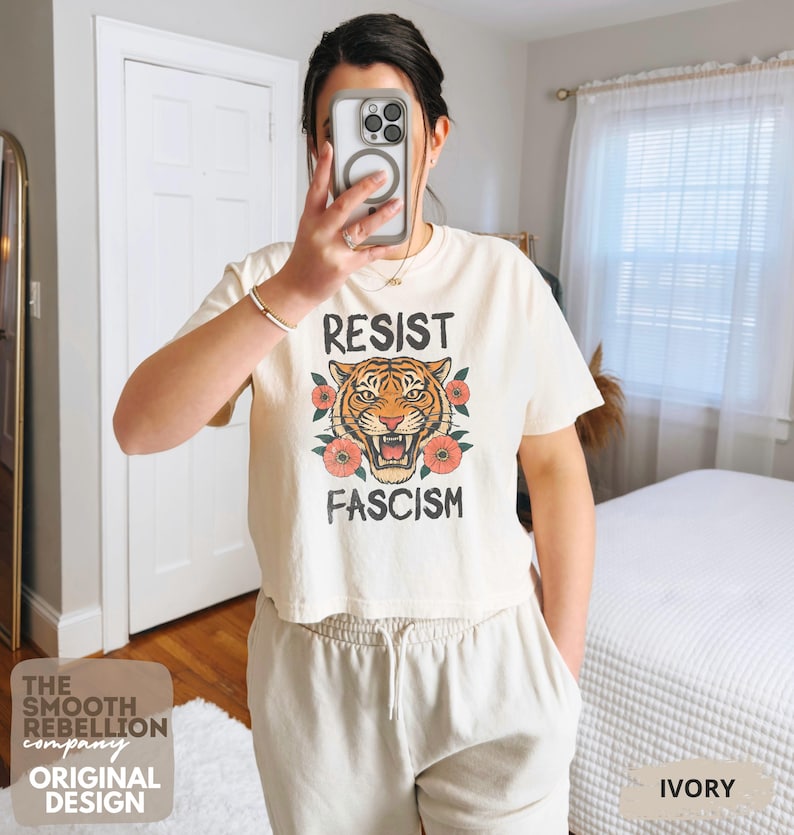 RESIST FASCISM Tiger Boxy T-Shirt for women. Political Protest Graphic Tee. Boxy tee that features a vintage-style painted tiger surrounded by vibrant poppies. Perfect for protests, marches, or just everyday defiance. Political merch for making a statement. Anti Trump top made for the loud and the politically engaged. Whether you're fighting fascism, defending democracy, or just making a statement. Short sleeves, crew neck. Boxy cropped tee. Very soft fabric. Printed in the US.