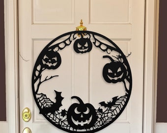 Może przedstawiać: Czarna metalowa wieniec halloweenowa z okrągłym wzorem przedstawiającym dynie, nietoperze i pajęczyny.